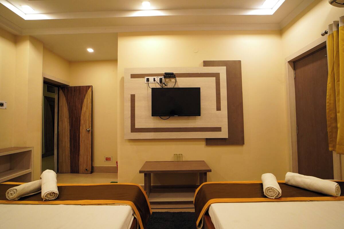 Habitación de hotel con dos camas, un televisor fijado a la pared, una mesita y una puerta que da a otra habitación.