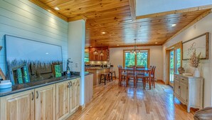 A spacious kitchen with wooden cabinets and a large island, a dining area with wooden chairs, and a ceiling with exposed beams. - Luxe Cabin at Bretton Woods (Carroll)