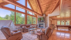 A spacious living room with a stone fireplace, large windows, and a pool table. - Luxe Cabin at Bretton Woods (Carroll)