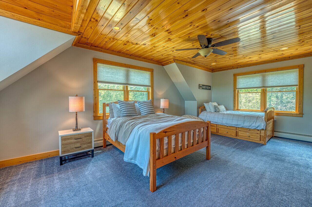 A bedroom with a sloped ceiling, two beds, a nightstand, and a window.