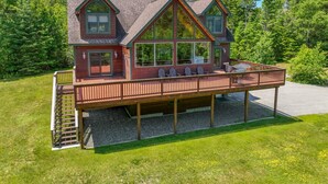 A two-story cabin with a deck, surrounded by a forest. - Luxe Cabin at Bretton Woods (Carroll)