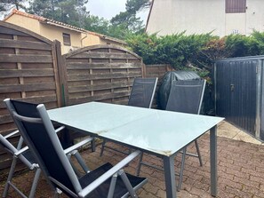 An outdoor patio with a table and chairs, a wooden fence, and a building in the background.