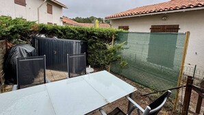 A patio with a table and chairs, a covered grill, and a fenced area with a green mesh.