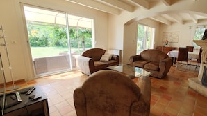 A spacious living room with a fireplace, two leather armchairs, a glass coffee table, and a dining area with a table and chairs.