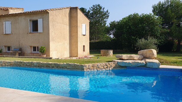 A house with a swimming pool, stone walls, and a patio area.