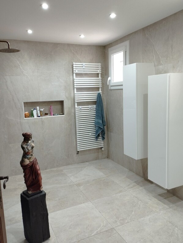 Une salle de bain moderne avec une douche, un porte-serviettes, une statue et une fenêtre.