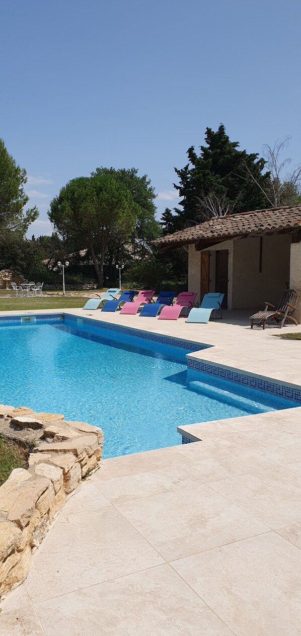 Une piscine avec des chaises longues, un mur en pierre et un bâtiment doté d’un toit en tuiles.