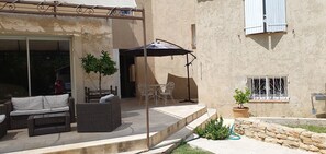 Une terrasse extérieure avec des meubles en osier, un espace salon couvert et une plante en pot.