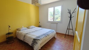 A bedroom with a bed, a bedside table, a lamp, a radiator, and a window.