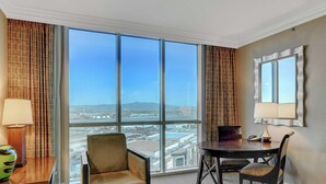 A hotel room with a large window, a round table, a chair, a lamp, and a mirror. - MGM Signature-Mountain View  Deluxe Spa 24th floor (Las Vegas)