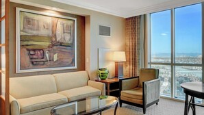 A hotel room with a large window, a sofa, a chair, a table, and a painting on the wall. - MGM Signature-Mountain View  Deluxe Spa 24th floor (Las Vegas)