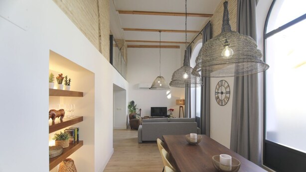 Interior moderno com piso de madeira, área de jantar com mesa e cadeiras de madeira, iluminação pendente e sala de estar com sofá e televisão.