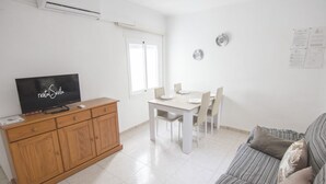 Un salon avec un téléviseur posé sur un meuble en bois, une table à manger avec des chaises et un canapé à rayures.