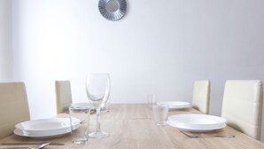 Une table à manger avec de l’assiette blanche, des verres transparents et des couverts, entourée de chaises de couleur beige.