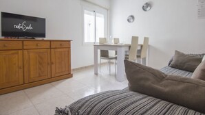 Un salon avec un canapé, un téléviseur posé sur un meuble en bois, une table à manger avec des chaises et une fenêtre.