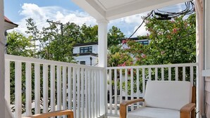 A covered outdoor area with a wooden bench and a cushioned chair, surrounded by a white fence. - Beautiful Penthouse Condo Just Steps to King (Charleston)