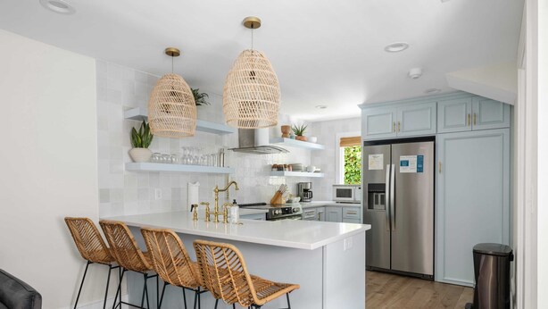 A modern kitchen with a central island, bar stools, hanging wicker lights, and stainless steel appliances. - Beautiful Penthouse Condo Just Steps to King (Charleston)