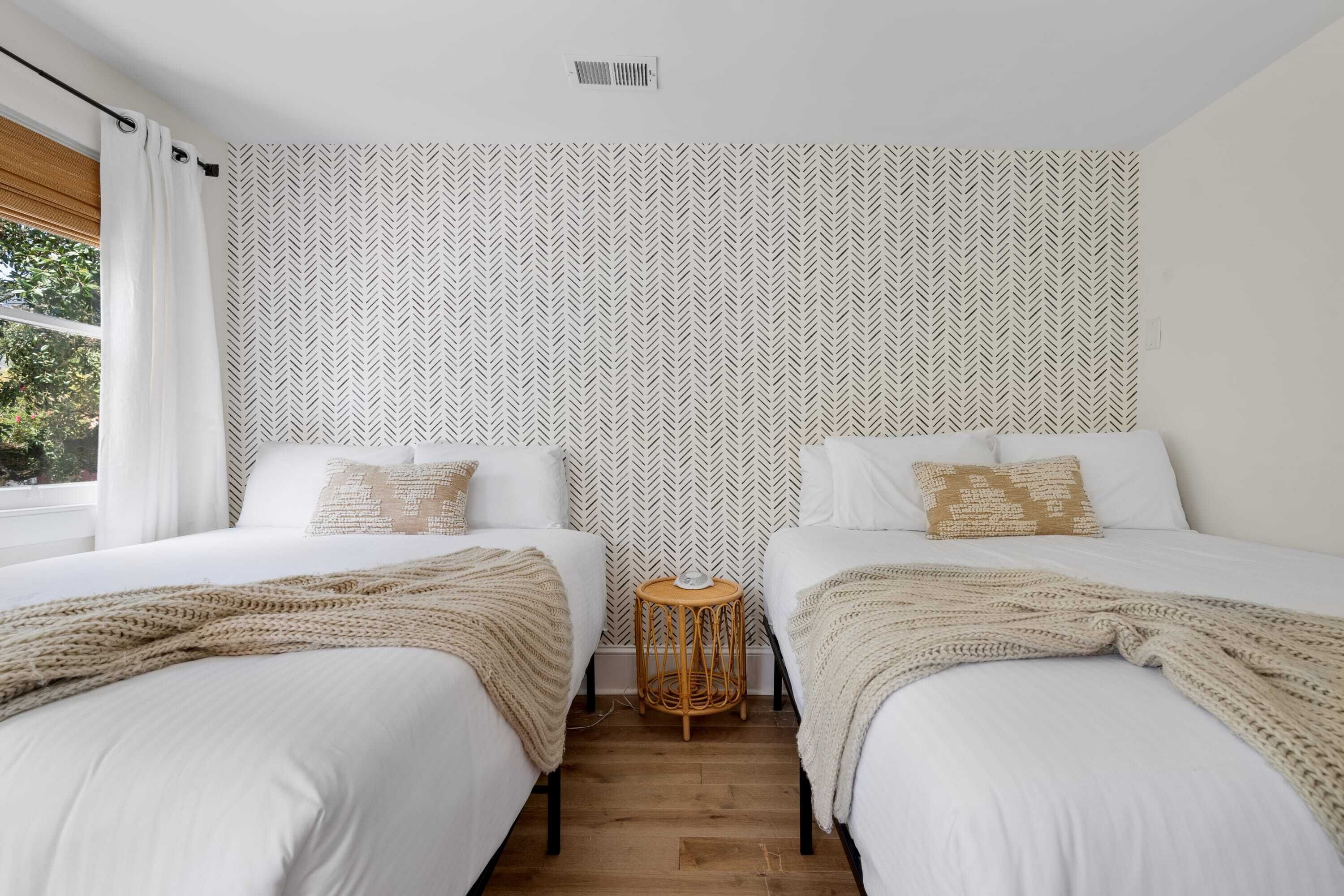 A hotel room with two beds, a small round table, and a patterned wall.