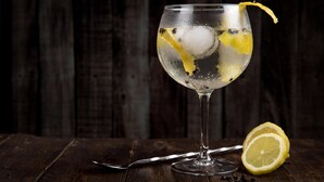 A glass of iced beverage with lemon slices and ice cubes, placed on a wooden surface with a spoon and a lemon half beside it. - Roomshala 084 Hotel Divine inn (Noida)