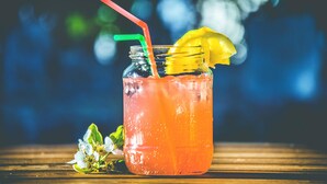 A glass with a red straw and a yellow slice garnish, placed on a wooden surface with blurred greenery in the background. - Roomshala 084 Hotel Divine inn (Noida)
