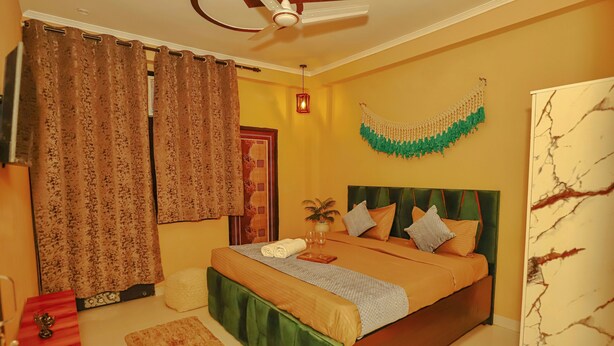 A bedroom with a bed, curtains, a ceiling fan, a wall decoration, and a bedside table. - Roomshala 084 Hotel Divine inn (Noida)