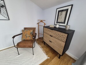 Une pièce comprenant une chaise, une commode en bois, un tableau encadré et un porte-manteau mural.