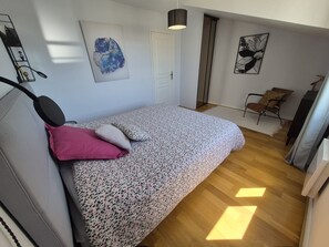 Ein Schlafzimmer mit Bett, Sessel, Tür und Bildern an den Wänden.