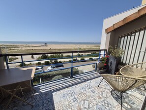 Ein Balkon mit Blick auf den Strand, ein Stuhl und ein Tisch.