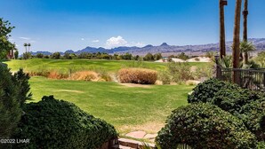 A golf course with a clear view of distant mountains, surrounded by lush greenery and palm trees. - Best location in Lake Havasu! Walk to London Bridge!  Heated Pool & Golf. (Lake Havasu City)