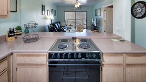 A kitchen with a central stove, wooden cabinets, and a dining area with a chair and table. - Best location in Lake Havasu! Walk to London Bridge!  Heated Pool & Golf. (Lake Havasu City)