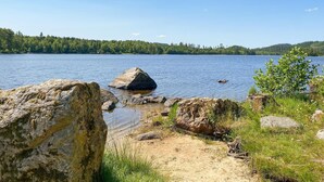 Ett vackert landskap med en sjö, en stenstrand och skogbeklädda kullar.