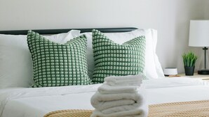 A neatly made bed with a yellow throw blanket, green patterned pillows, and a stack of white towels. - Guests book because it's convenient. They return because it feels effortless. (Montgomery)