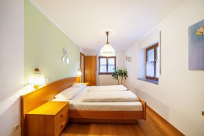 Een slaapkamer met een houten bed, nachtkastjes, een hanglamp, een raam met gordijnen en een kleine plant.