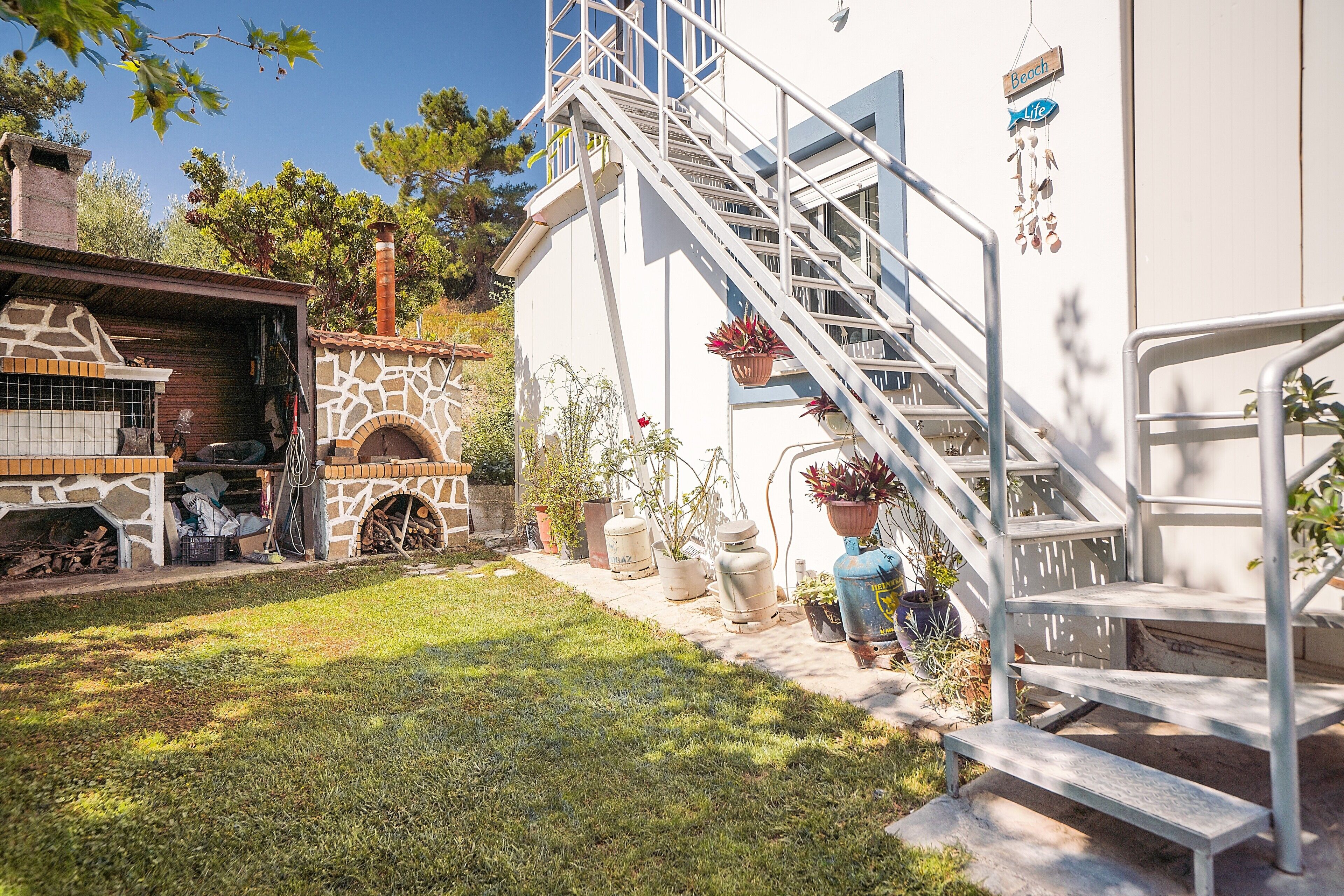 Une maison avec une cheminée en pierre, un escalier et des plantes en pot.