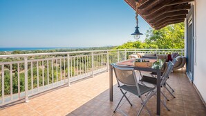 Ein Balkon mit Tisch und Stühlen, einer hängenden Leuchte und Blick auf die Landschaft.