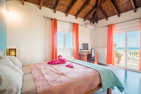 A bedroom with a bed, a desk, a chair, and a view of the sea.