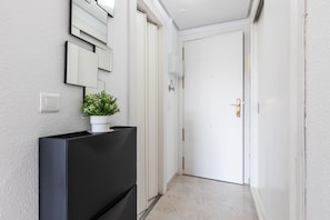 A hallway with a black cabinet, a potted plant, a white door, and a wall-mounted light switch.