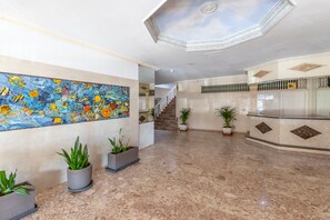 A lobby with a large colorful mural, a reception desk, potted plants, and a staircase.