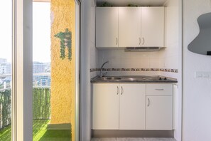 Cocina compacta con armarios blancos, un lavamanos de acero inoxidable y un salpicadero de azulejos.