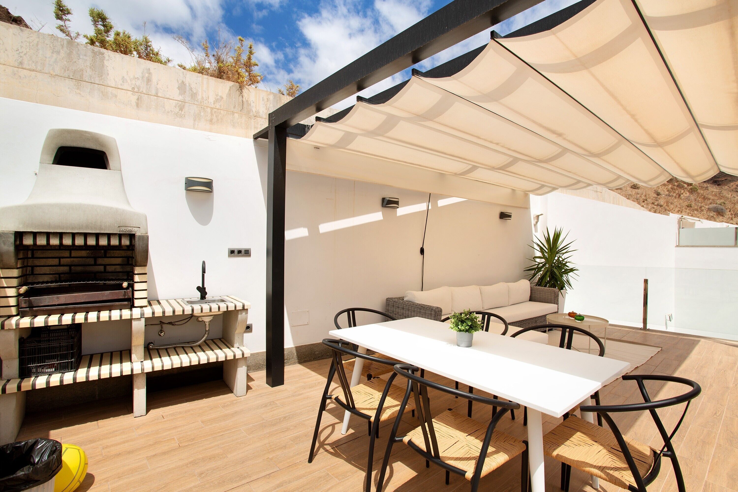 An outdoor patio with a white table, chairs, a barbecue grill, and a covered seating area.