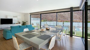A modern living room with a glass dining table, teal sofa, and a large TV. - Villa "Tauro 31" with Sea Views, Private Pool, and Wi-Fi (Mogán)
