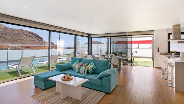 A modern living room with a sofa, a coffee table, and a view of a pool and mountains. - Villa "Tauro 31" with Sea Views, Private Pool, and Wi-Fi (Mogán)