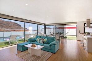 Ein modernes Wohnzimmer mit Sofa, Couchtisch und Blick auf Pool und Berge.