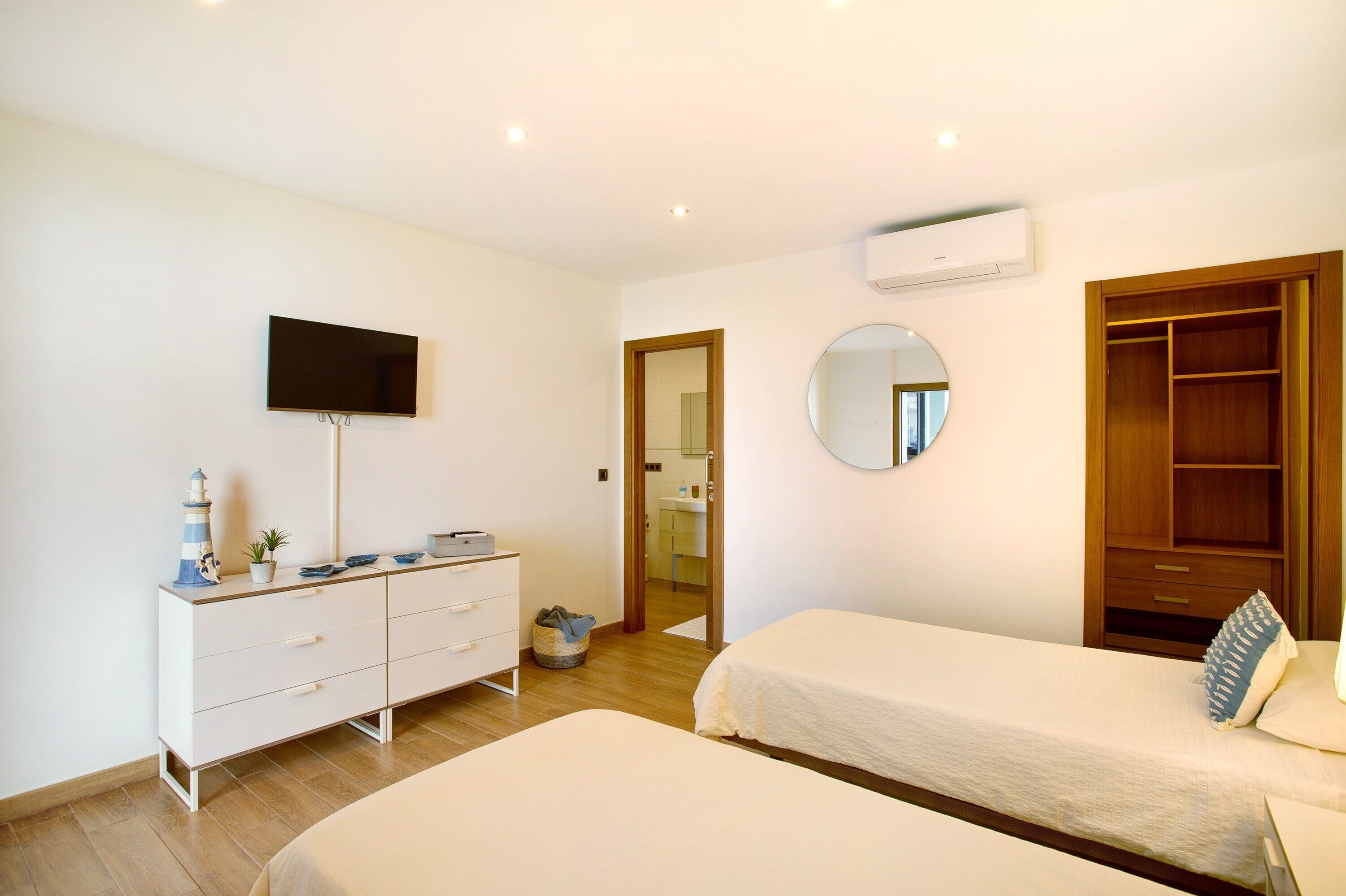 A bedroom with two beds, a TV, a dresser, a mirror, and a wooden wardrobe.
