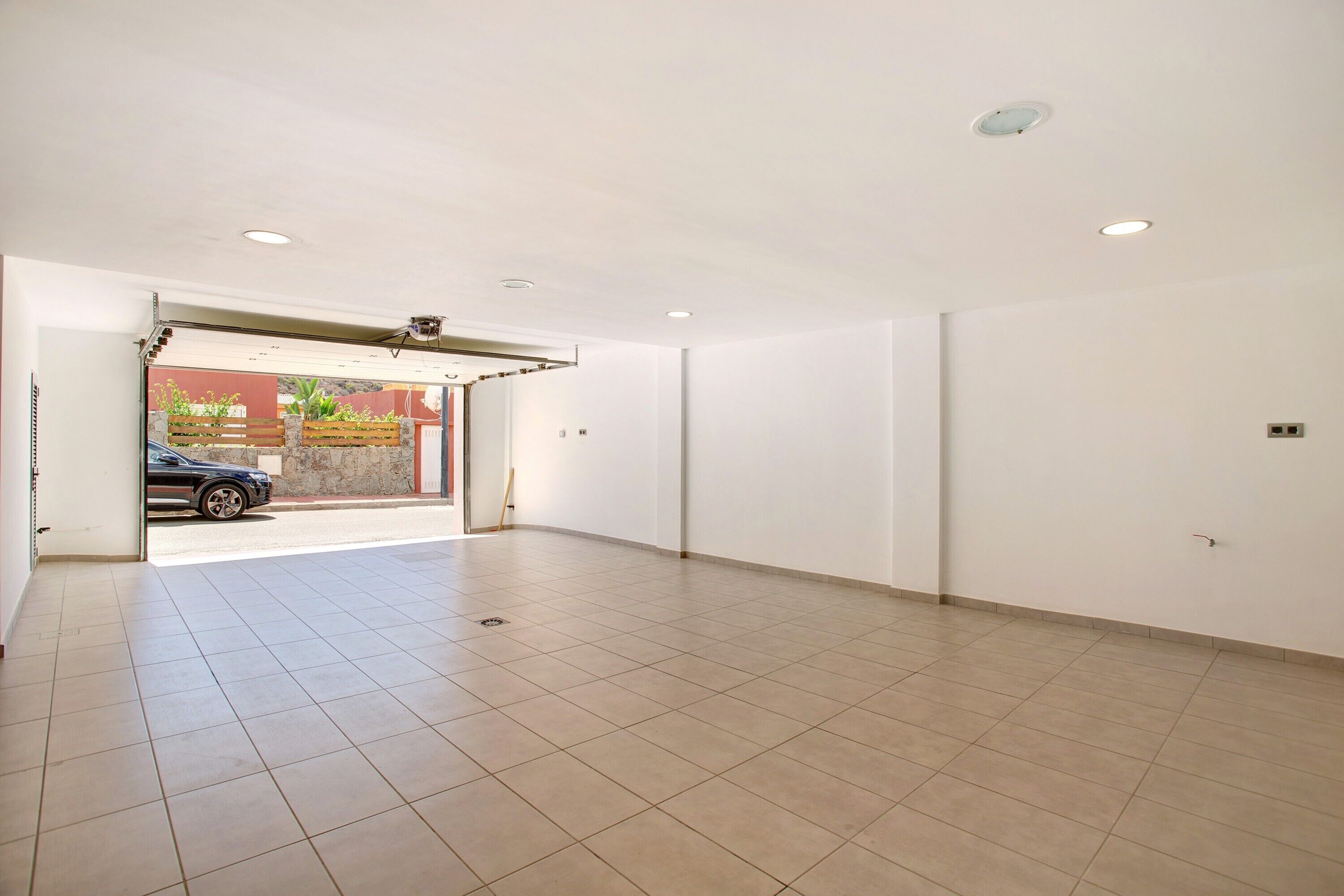A spacious room with a tiled floor, a door leading outside, and a ceiling with recessed lighting.