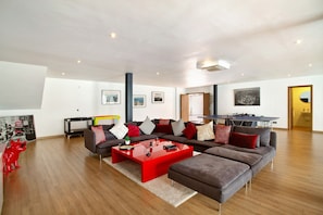 A spacious living room with a large sectional sofa, a red coffee table, and a ping pong table in the background. - Villa "Tauro 31" with Sea Views, Private Pool and Wi-Fi (Mogán)
