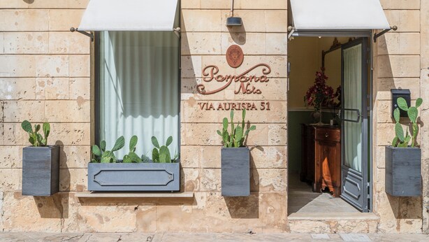 Une façade d’immeuble avec une enseigne indiquant « Penina Nobile » et « VIA AURISPA 51 ». Deux cactus en pot sont placés sur les rebords des fenêtres.