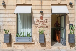 Facciata di un edificio con un cartello che riporta 'Penina Nobile' e 'VIA AURISPA 51'. Due cactus in vaso sui davanzali.