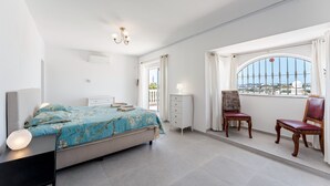 Une chambre à coucher avec un lit, une table de chevet, une lampe, une chaise et une fenêtre donnant sur un beau paysage.