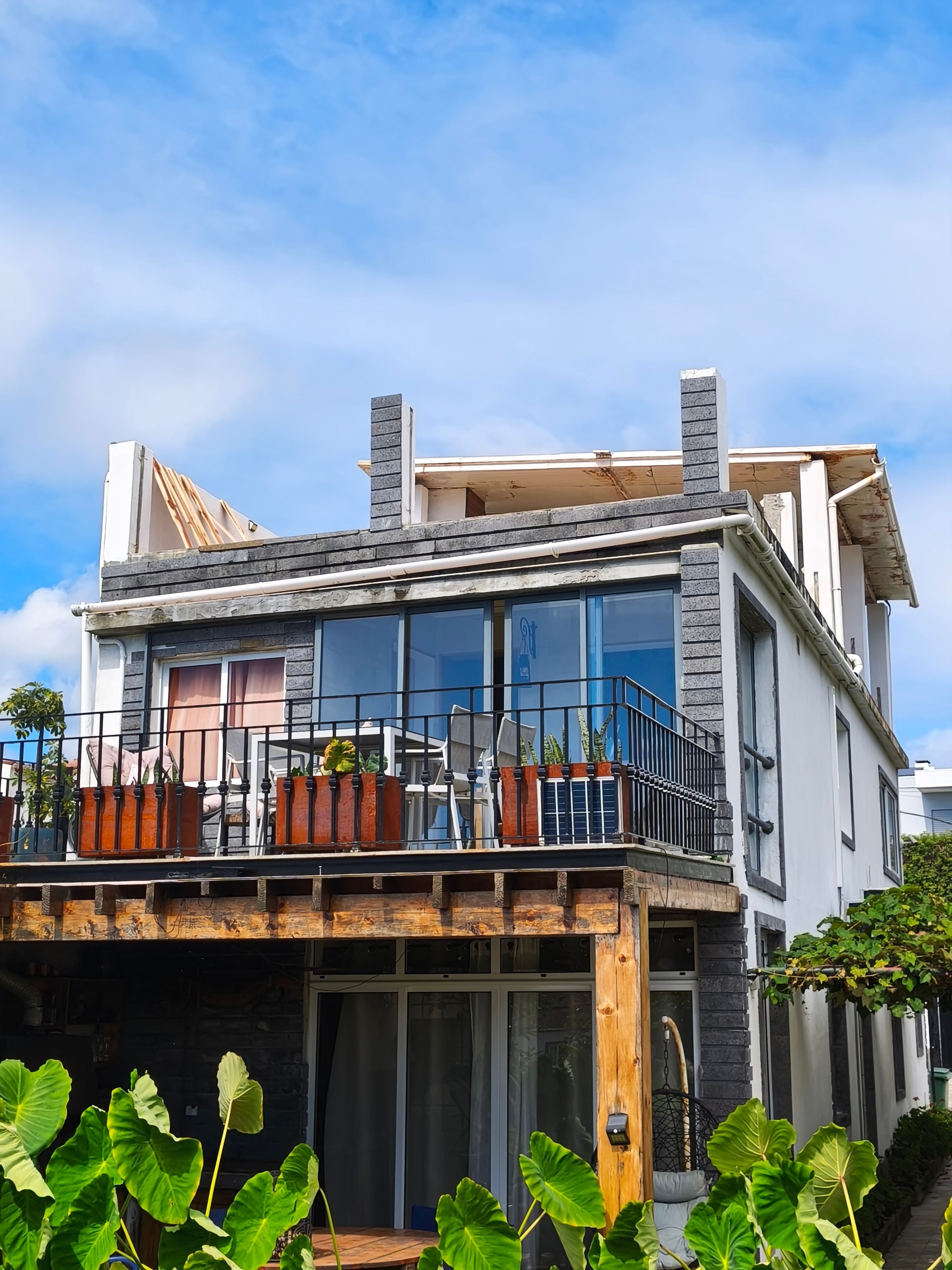 Une maison moderne à deux étages, dotée d’un balcon, de grandes fenêtres et de plantes en pot.